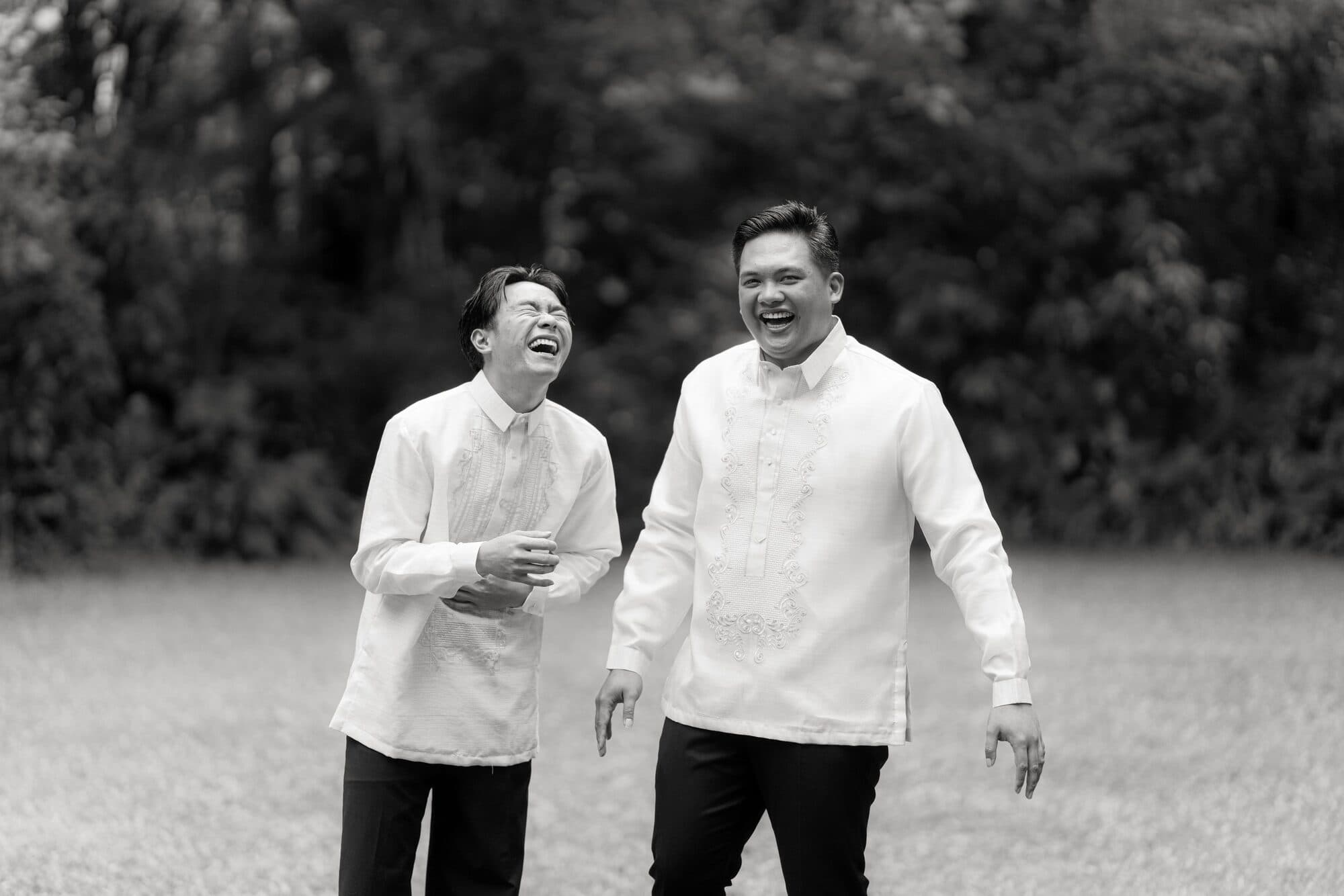 The groom and a friend in barongs walking across the lawn, both of them laughing
