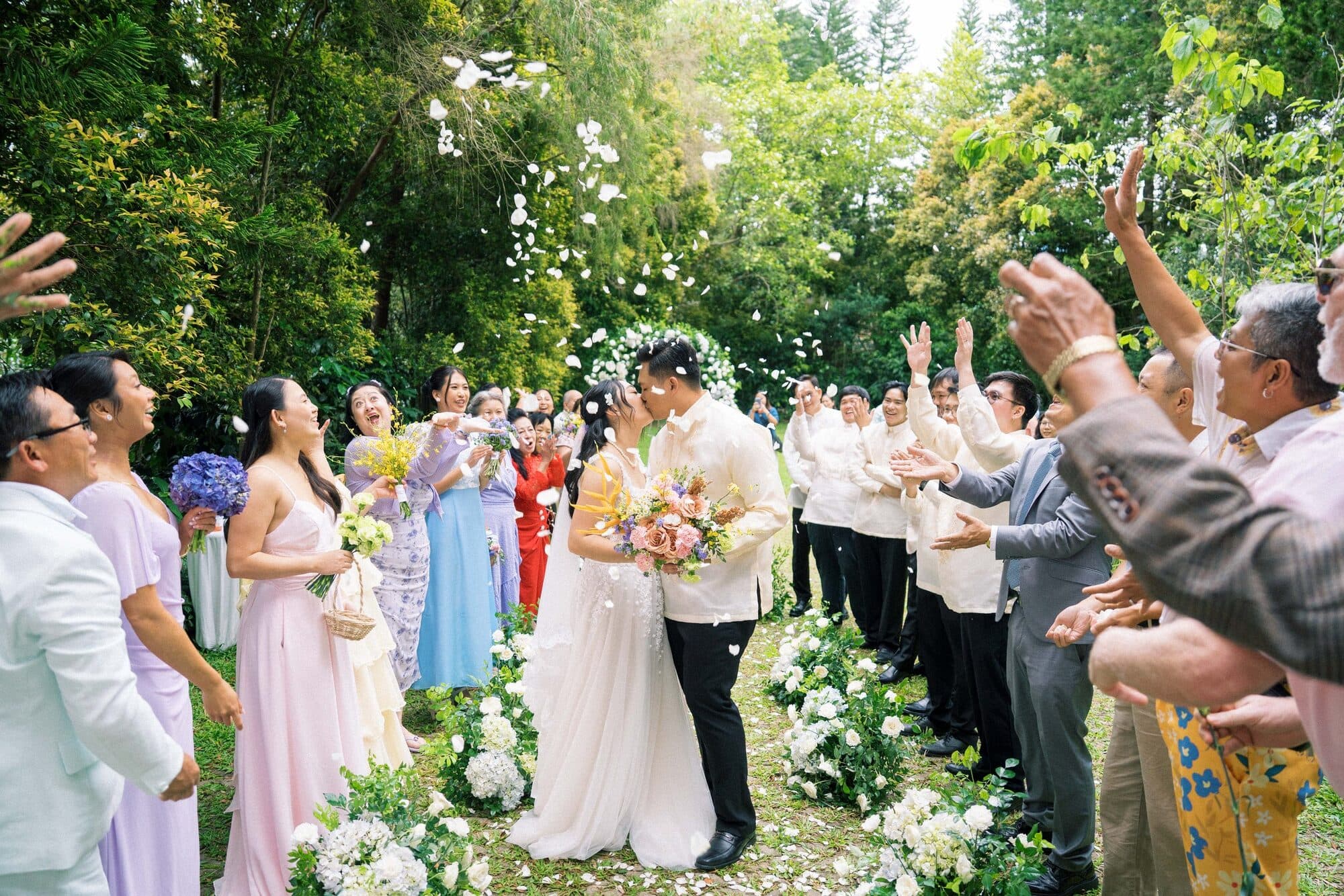 The newlyweds kissing in a shower of petals as guests cheer on either side of the garden aisle