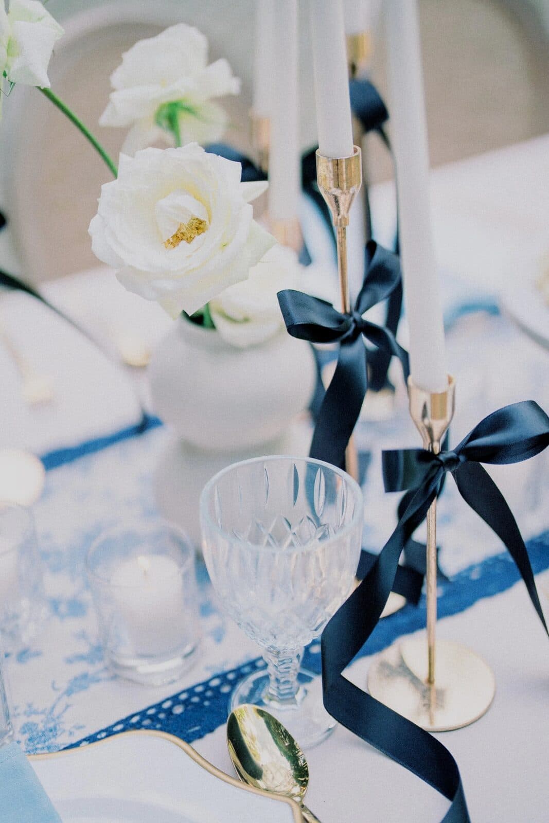 A reception table set with white roses, candles and navy ribbons